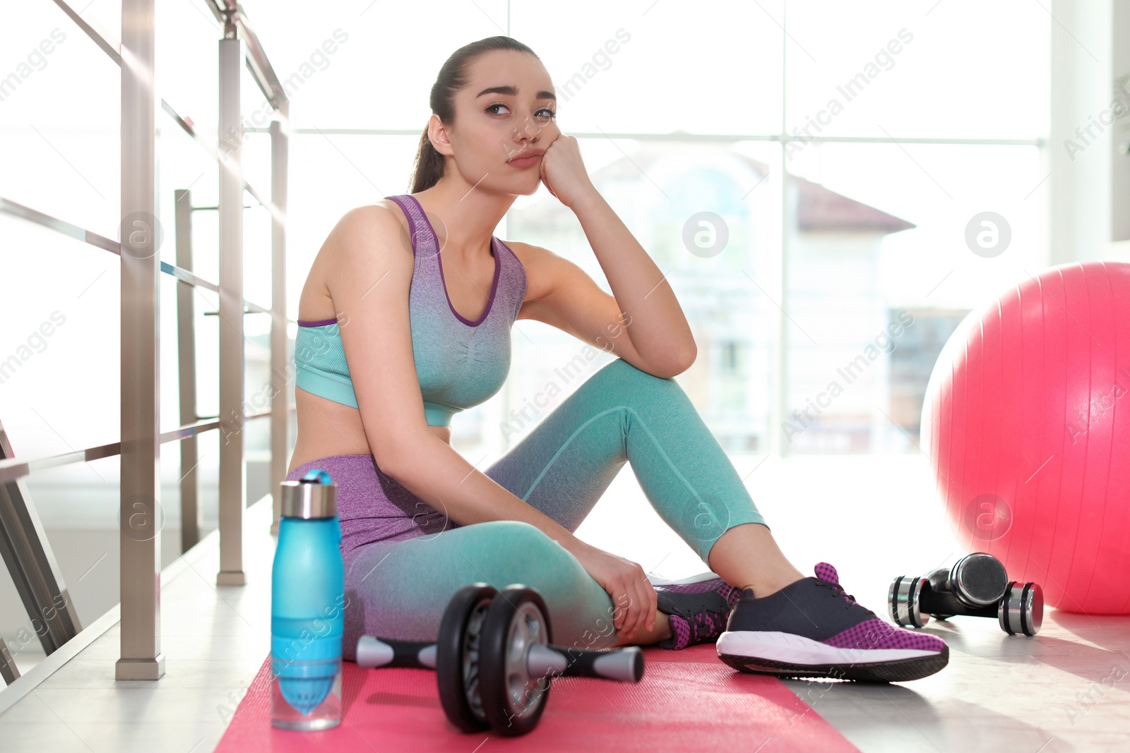 Photo of Lazy young woman with sport equipment on yoga mat indoors