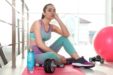 Lazy young woman with sport equipment on yoga mat indoors