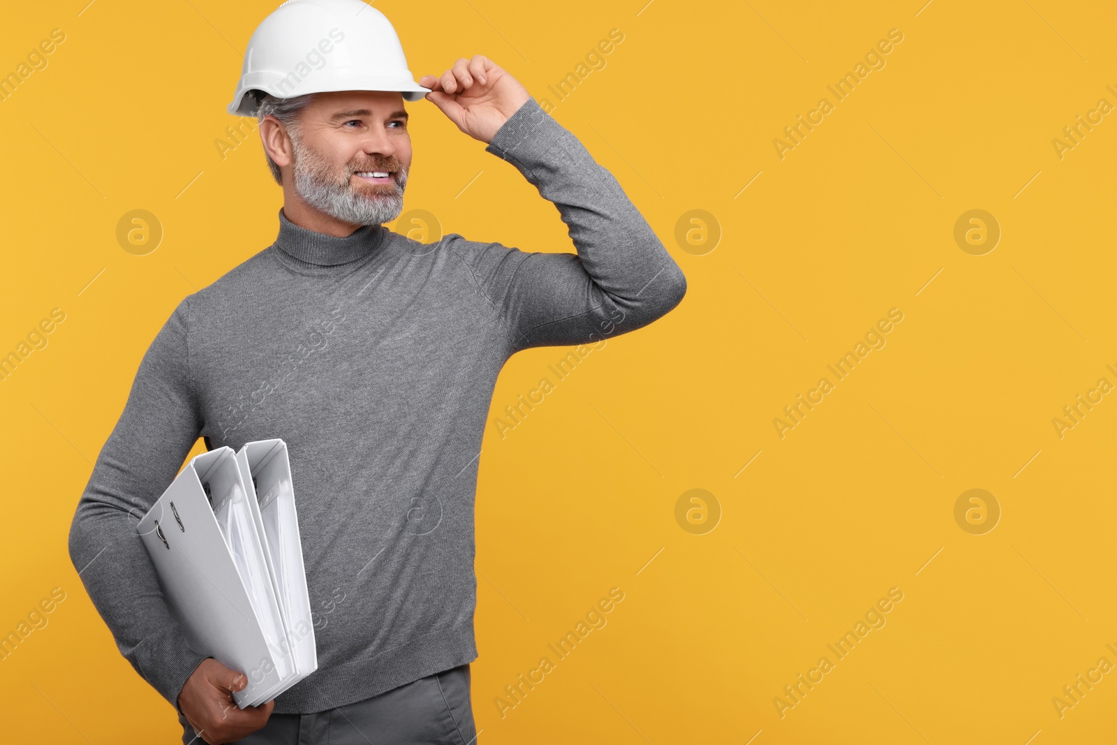 Photo of Architect in hard hat holding folders on orange background. Space for text