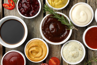 Different tasty sauces in bowls and ingredients on wooden table, flat lay