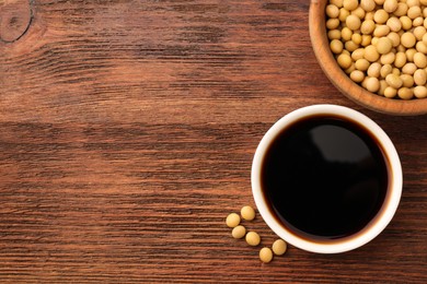 Soy sauce in bowl and soybeans on wooden table, flat lay. Space for text