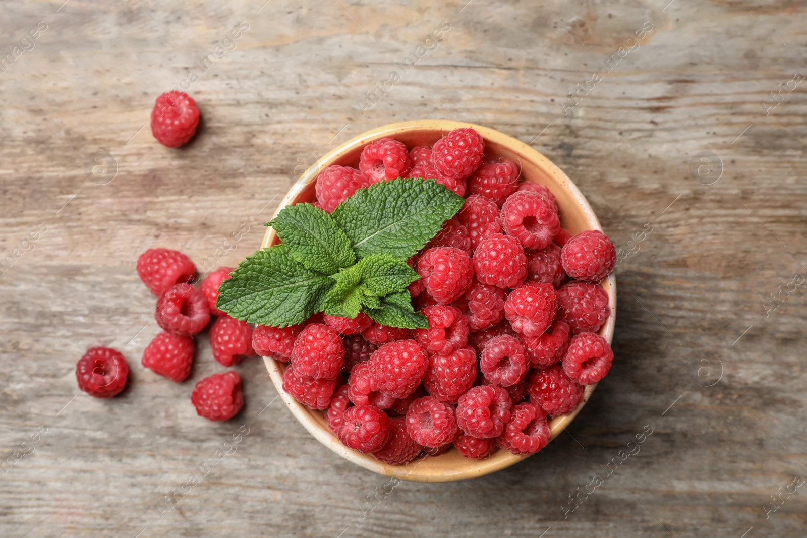 Photo of Bowl with ripe aromatic raspberries on wooden table, top view