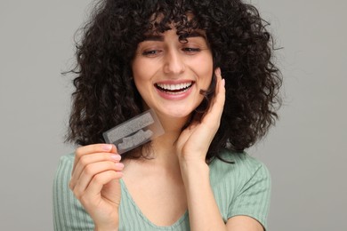 Photo of Young woman holding teeth whitening strips on grey background