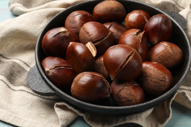 Photo of Fresh edible sweet chestnuts in frying pan on table, closeup