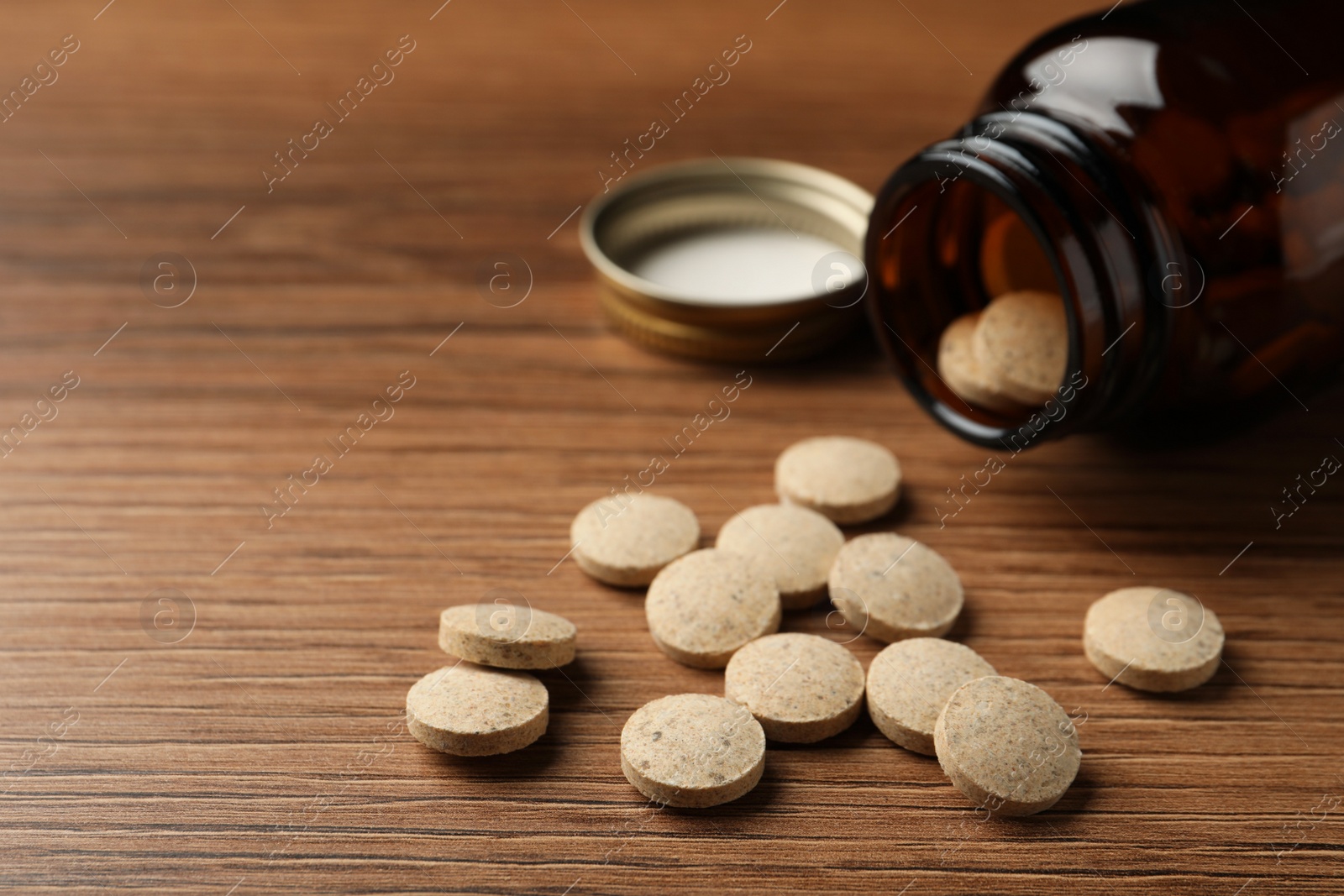 Photo of Overturned bottle with dietary supplement pills on wooden table, closeup