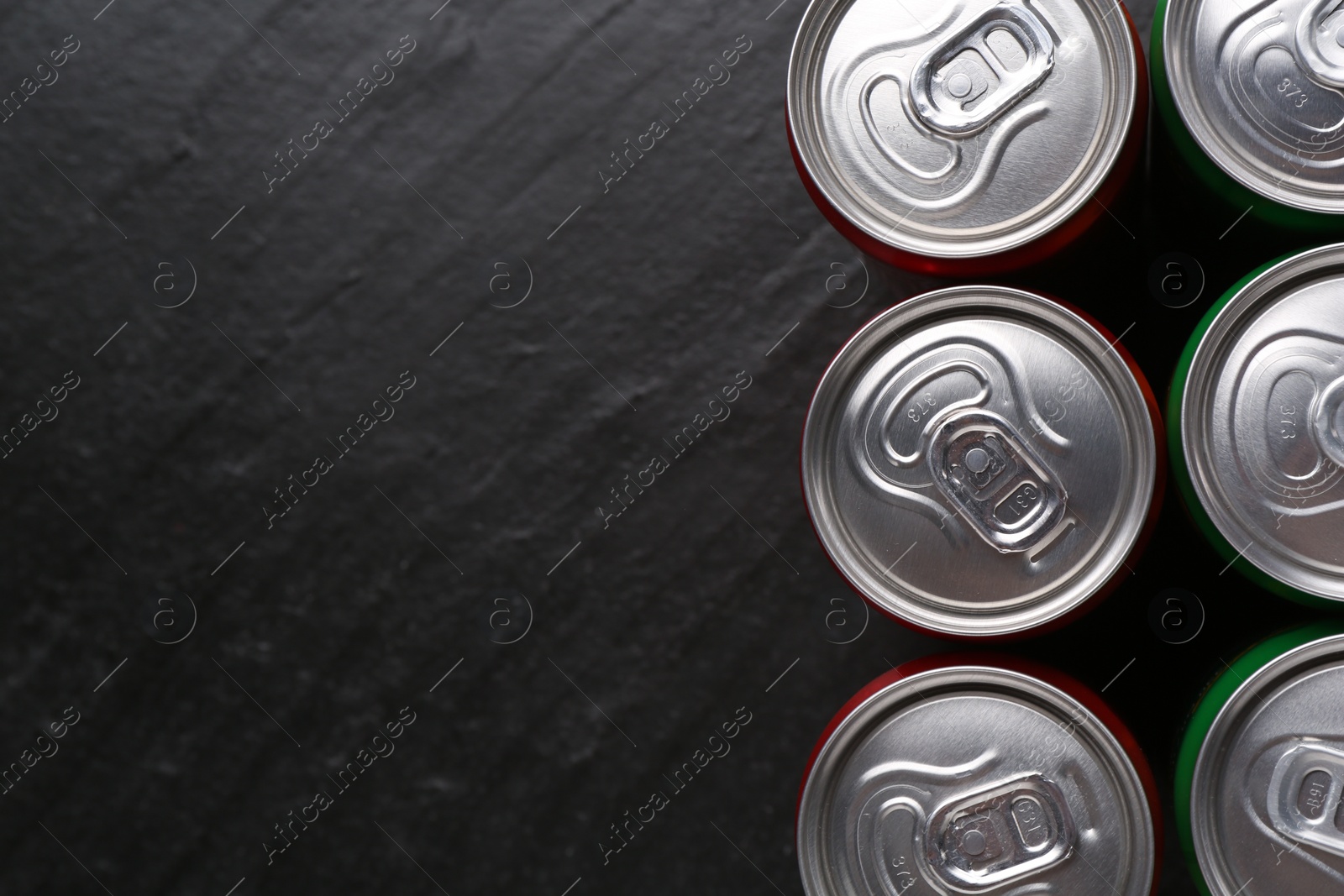 Photo of Energy drink in cans on black textured background, top view. Space for text