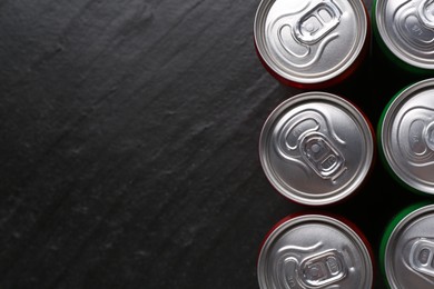 Photo of Energy drink in cans on black textured background, top view. Space for text