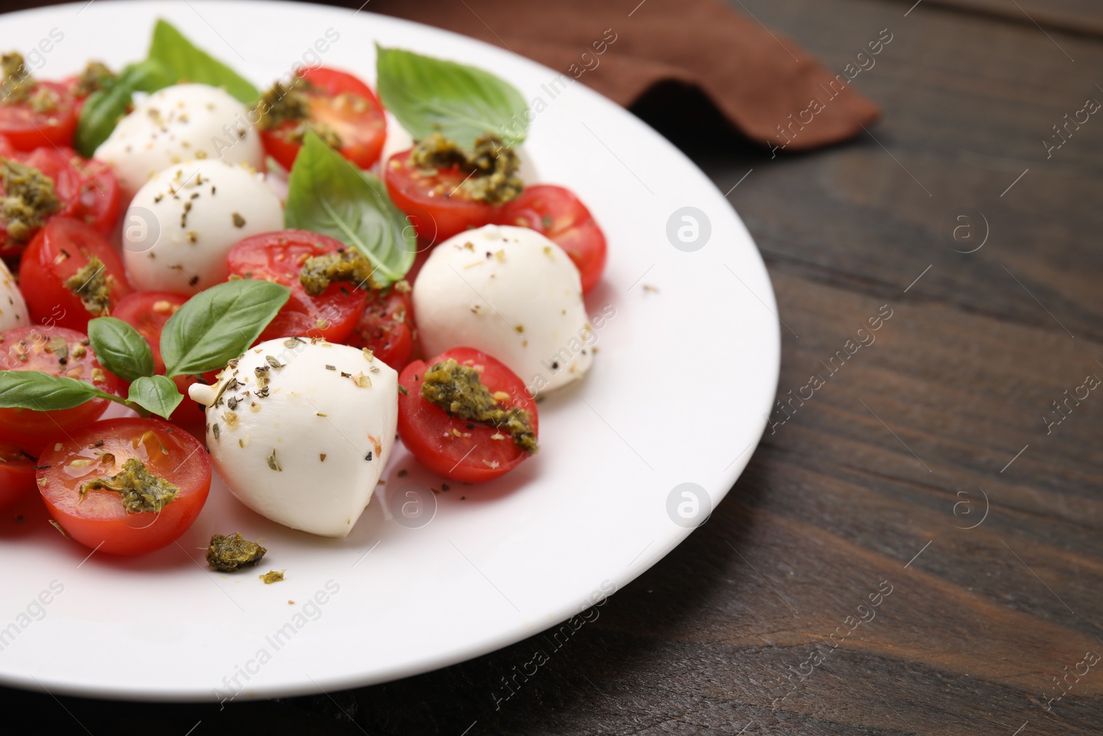Photo of Tasty salad Caprese with tomatoes, mozzarella balls and basil on wooden table, closeup. Space for text