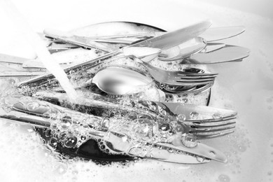 Photo of Washing silver spoons, forks and knives under stream of water in kitchen sink, closeup
