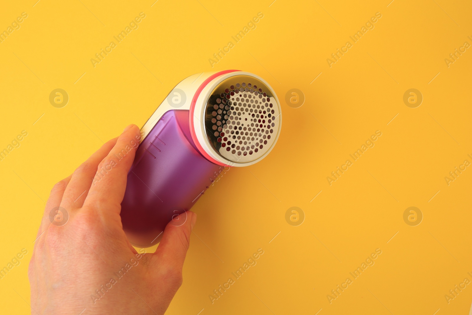 Photo of Woman holding modern fabric shaver on yellow background, closeup. Space for text