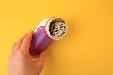 Woman holding modern fabric shaver on yellow background, closeup. Space for text