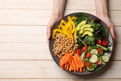 Photo of Balanced diet and vegetarian foods. Woman holding plate with different delicious products at wooden table, top view. Space for text