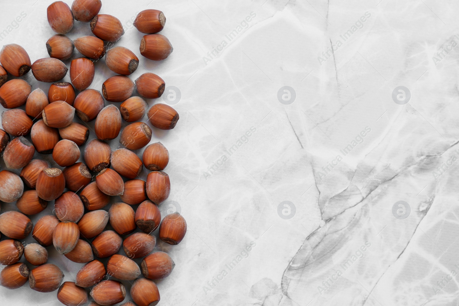 Photo of Pile of tasty hazelnuts on light marble table, top view. Space for text