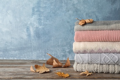 Photo of Stack of warm clothes with autumn leaves on wooden table. Space for text