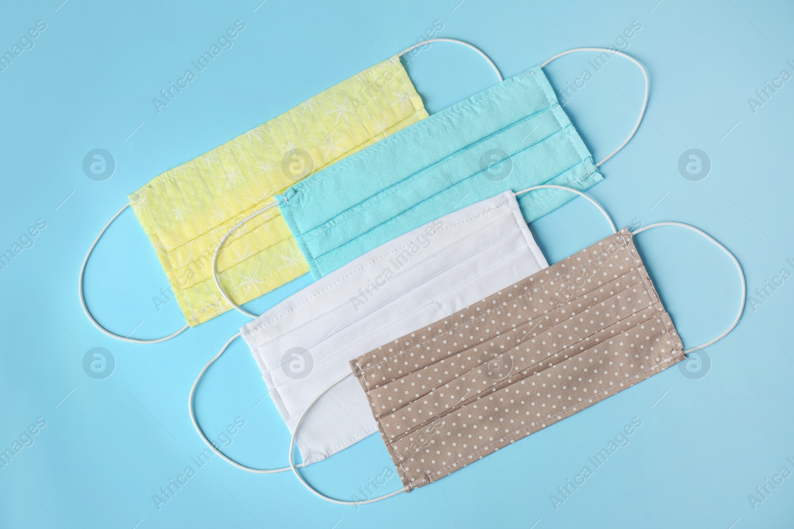 Photo of Homemade protective face masks on light blue background, flat lay