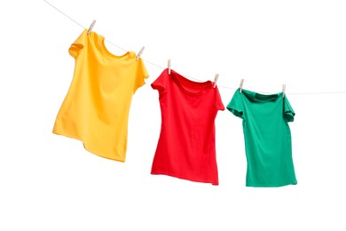 Photo of Different bright t-shirts drying on washing line against white background