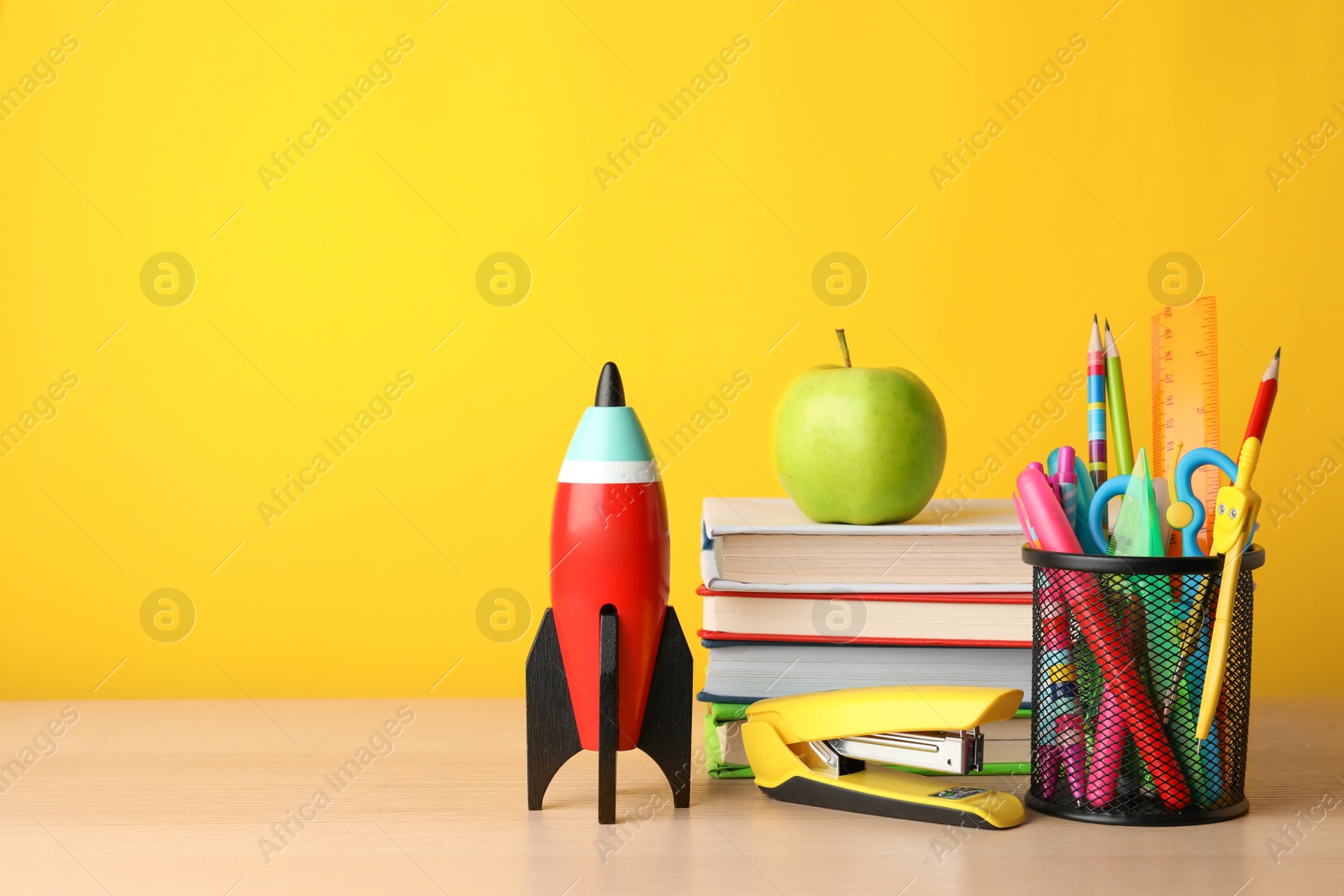 Photo of Bright toy rocket and school supplies on wooden table. Space for text