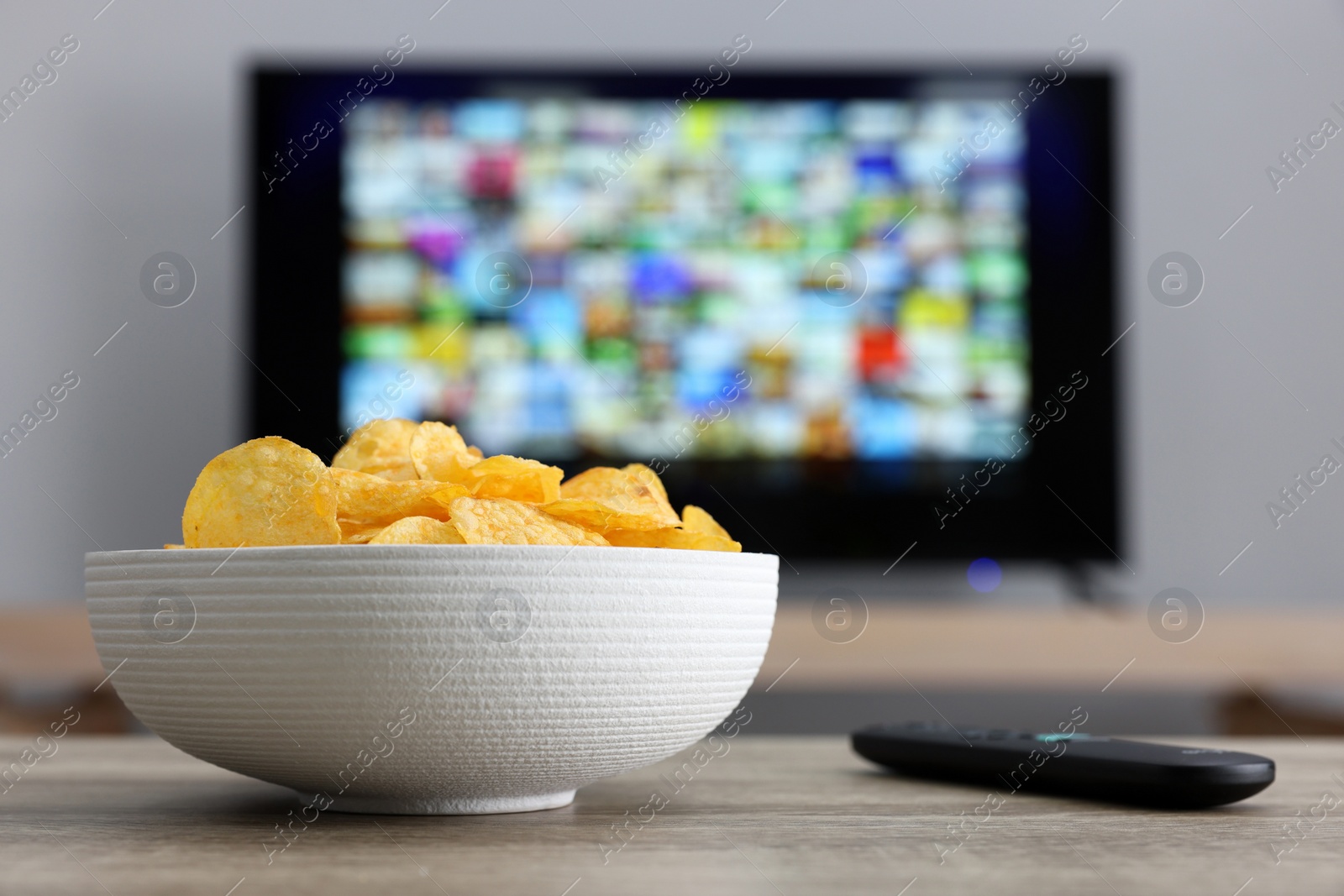 Photo of Bowl of chips and TV remote control on table indoors