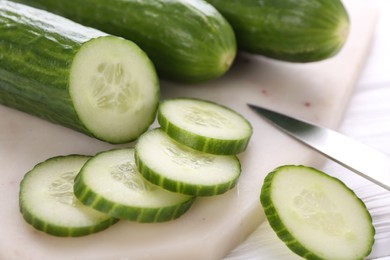 Photo of Cucumbers, knife and marble cutting board on white table, closeup