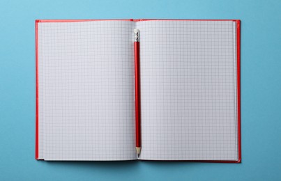 Photo of Open notebook with blank sheets and pencil on light blue background, top view