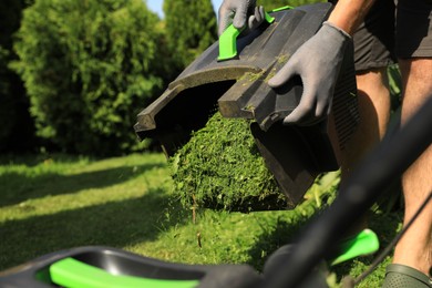 Man removing grass out of lawn mower box in garden, closeup