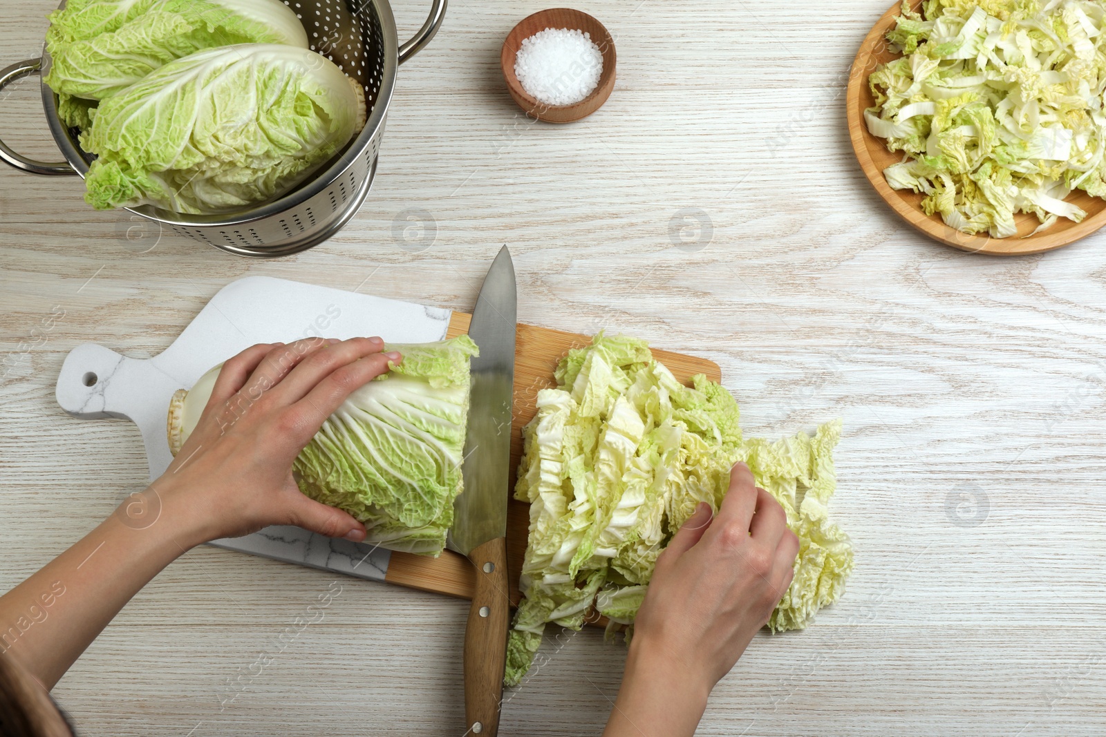 Photo of Woman cutting Chinese cabbage at white wooden kitchen table, top view