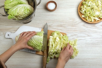 Photo of Woman cutting Chinese cabbage at white wooden kitchen table, top view