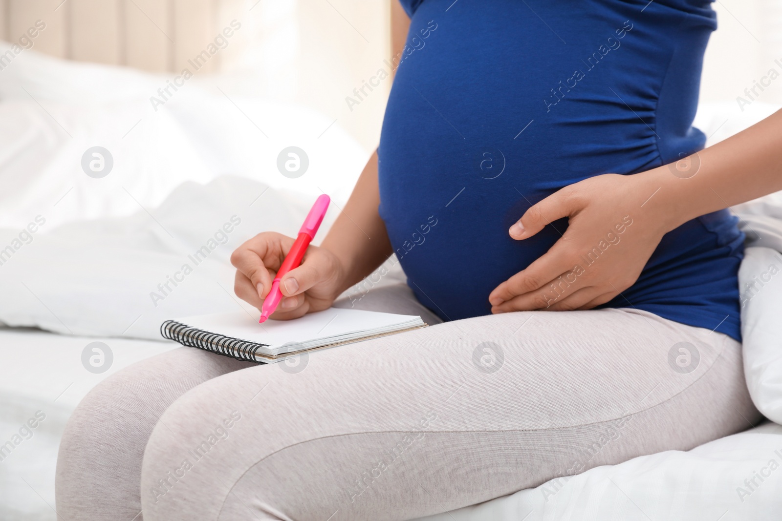 Photo of Pregnant woman with notebook and marker choosing name for baby on bed, closeup