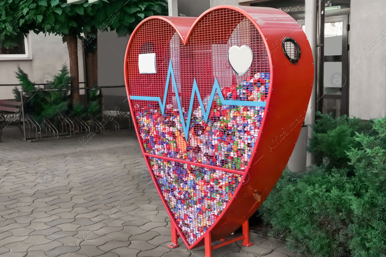 Photo of Heart shaped red recycling container for plastic caps outdoors