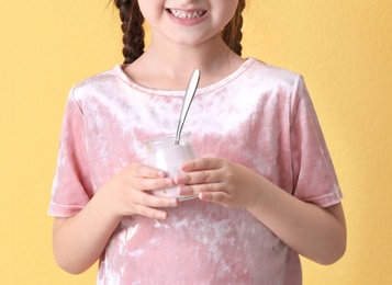 Little girl with yogurt on color background, closeup