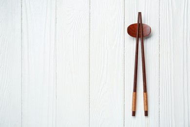 Photo of Pair of chopsticks with rest on white wooden table, top view. Space for text