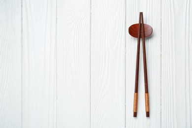 Pair of chopsticks with rest on white wooden table, top view. Space for text