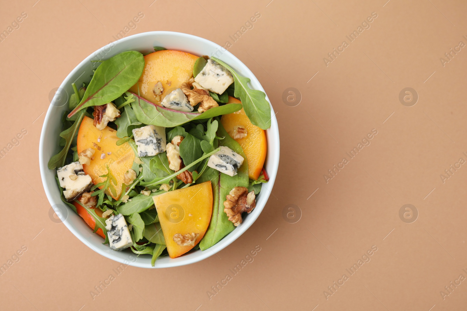 Photo of Tasty salad with persimmon, blue cheese and walnuts served on light brown background, top view. Space for text