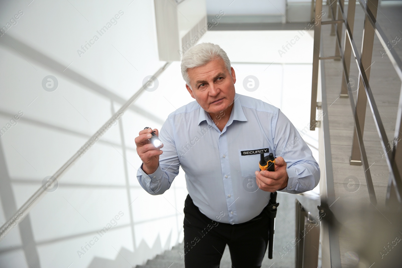 Photo of Professional security guard with flashlight and portable radio set on stairs