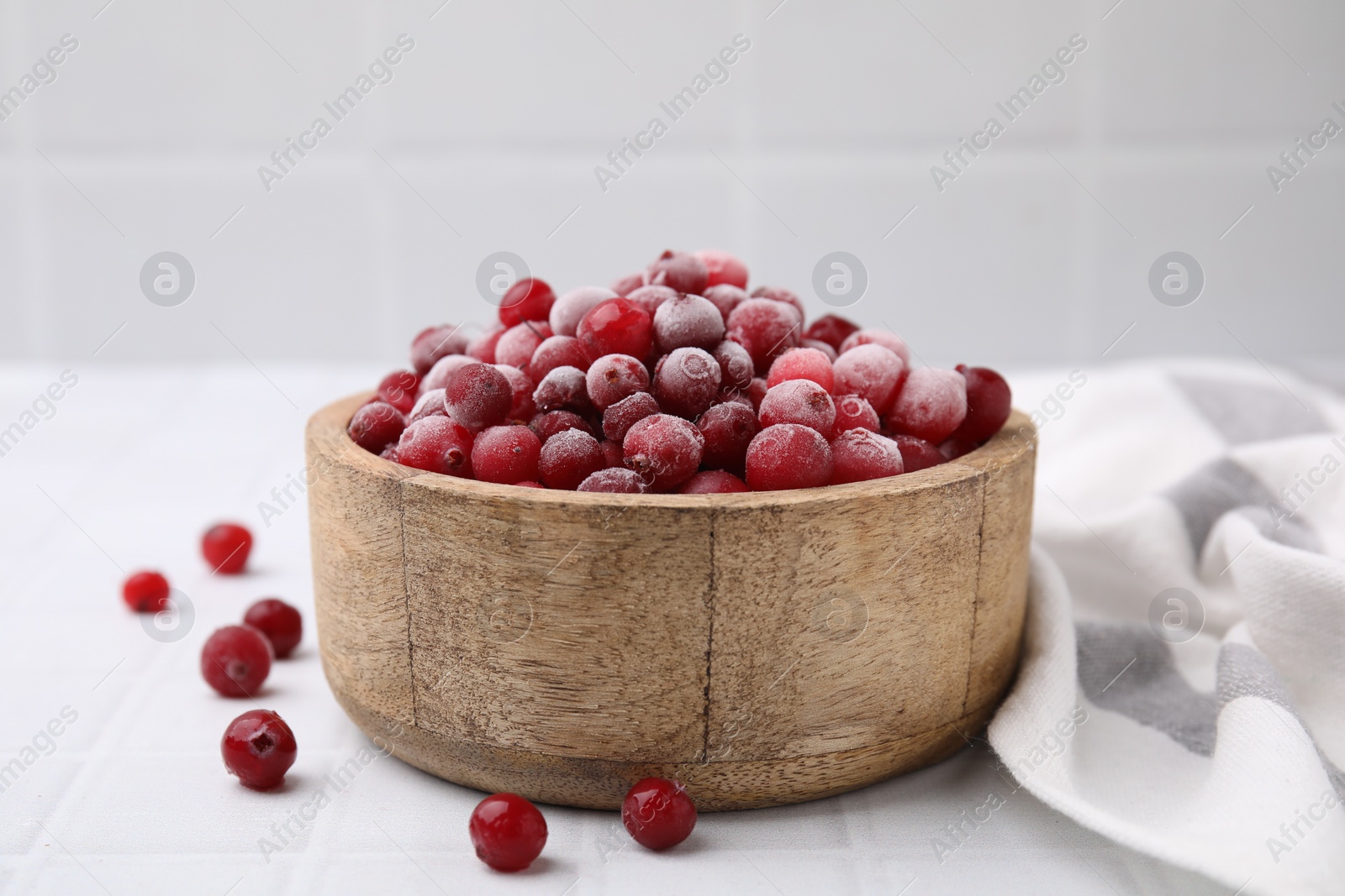 Photo of Frozen red cranberries in bowl on white tiled table, closeup