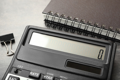 Photo of Calculator, notebook and paper clip on grey table, closeup. Tax accounting
