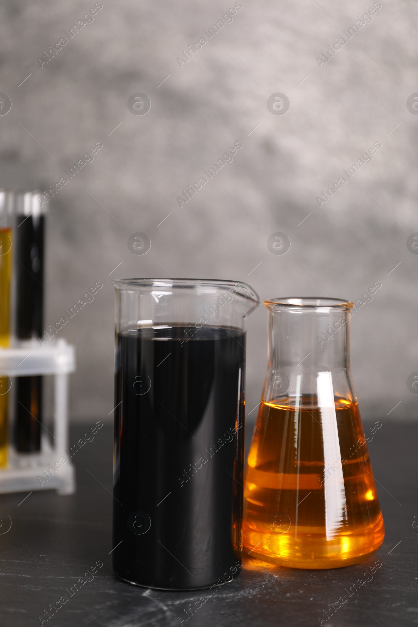 Photo of Beaker, flask and test tubes with different types of oil on grey textured table