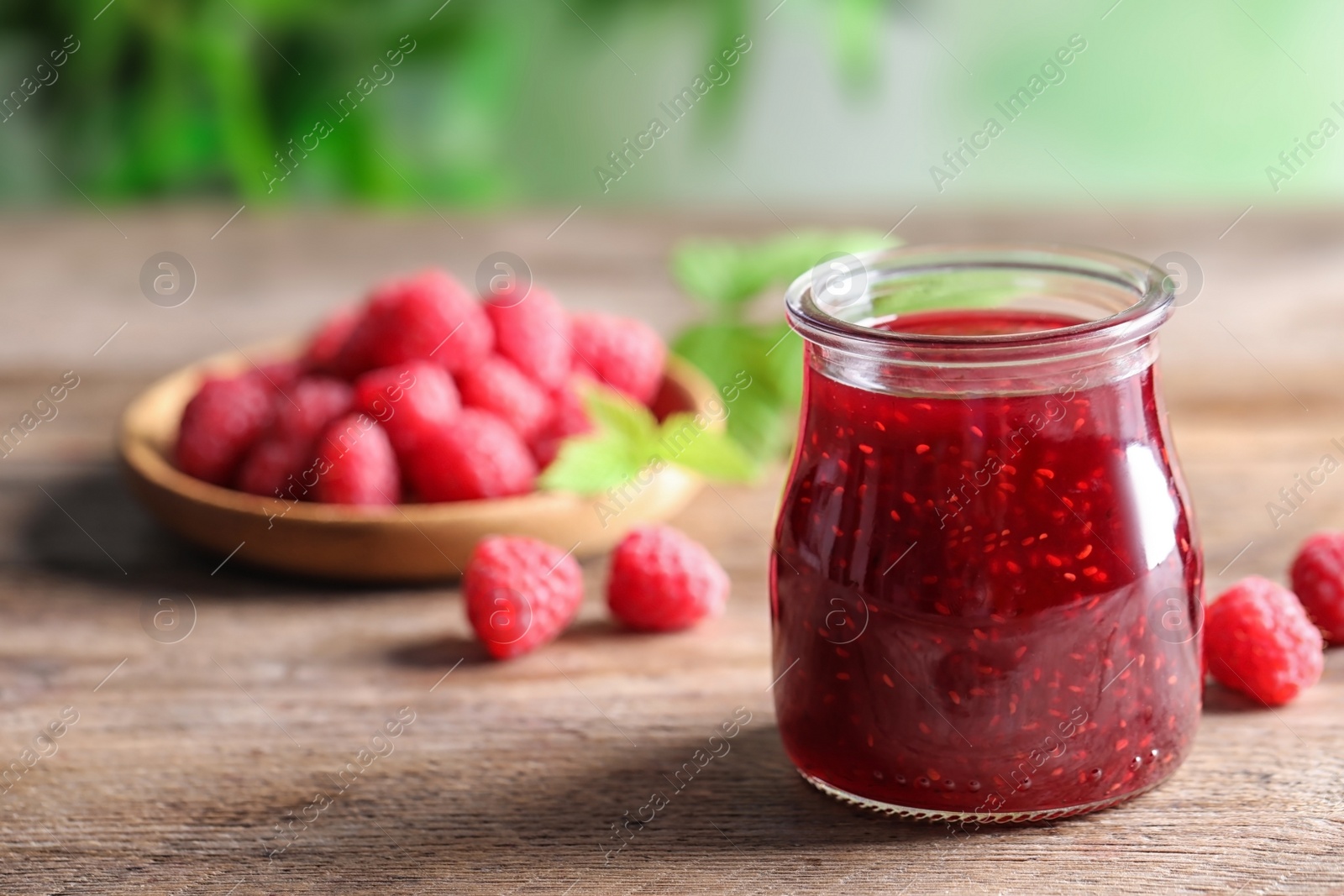 Photo of Glass jar of sweet jam with ripe raspberries on wooden table. Space for text