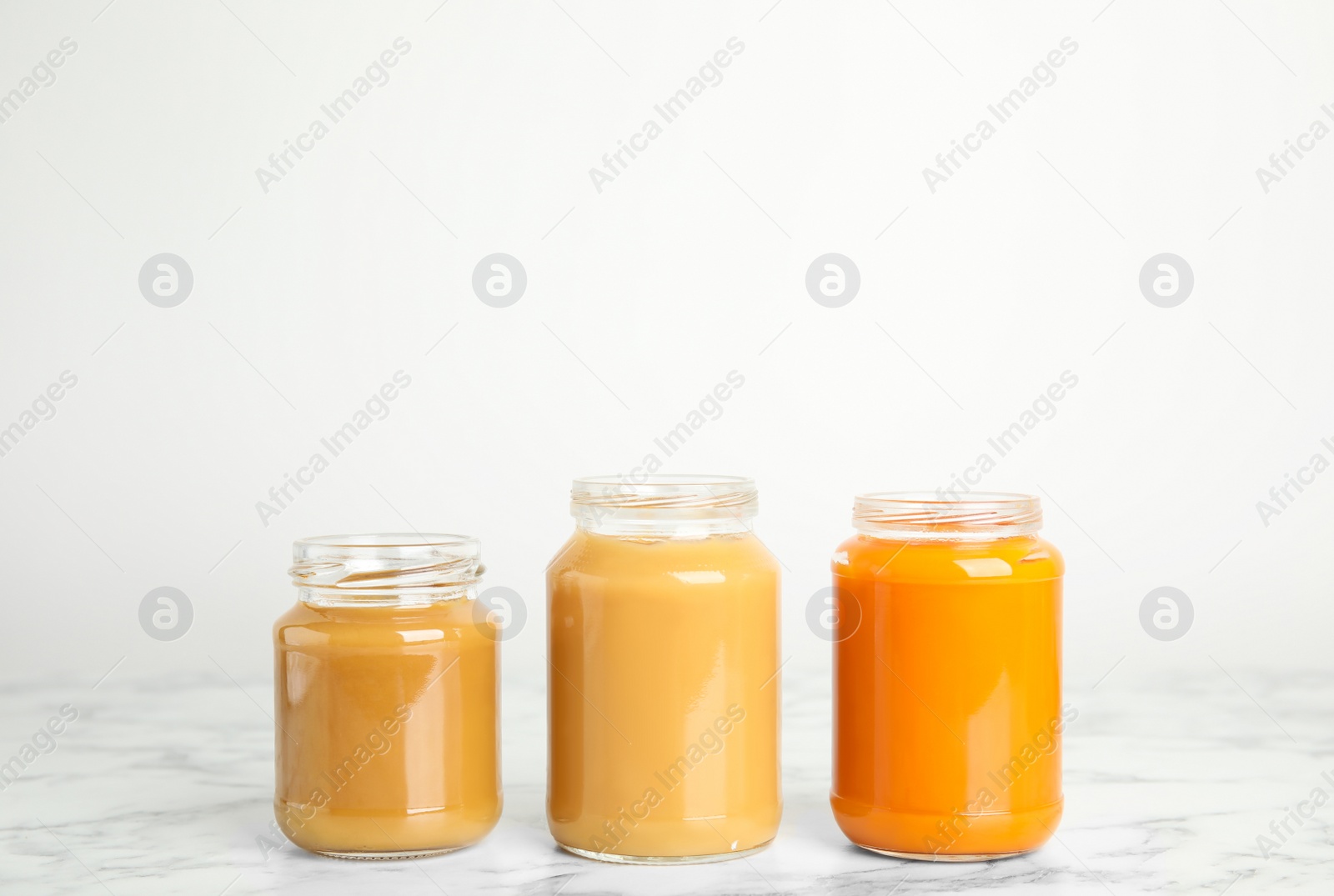 Photo of Healthy baby food in jars on marble table against white background