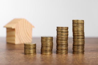 Photo of Mortgage concept. House model and stacks of coins on wooden table against white background, selective focus