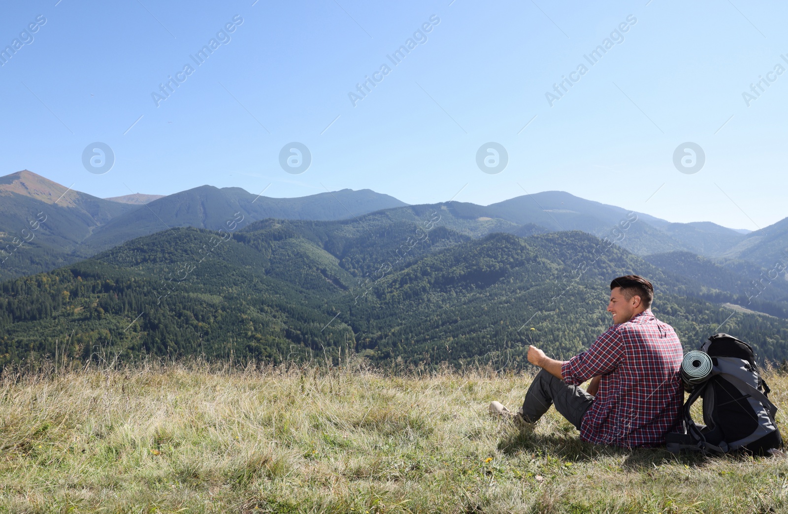 Photo of Tourist with backpack sitting on ground and enjoying view in mountains