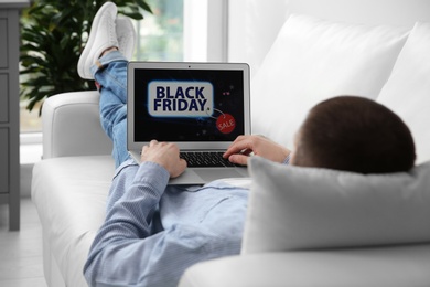 Photo of Man shopping online using laptop on couch at home, closeup. Black Friday Sale