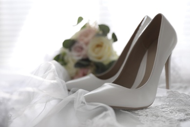 Photo of Pair of white high heel shoes, veil and wedding bouquet on light background