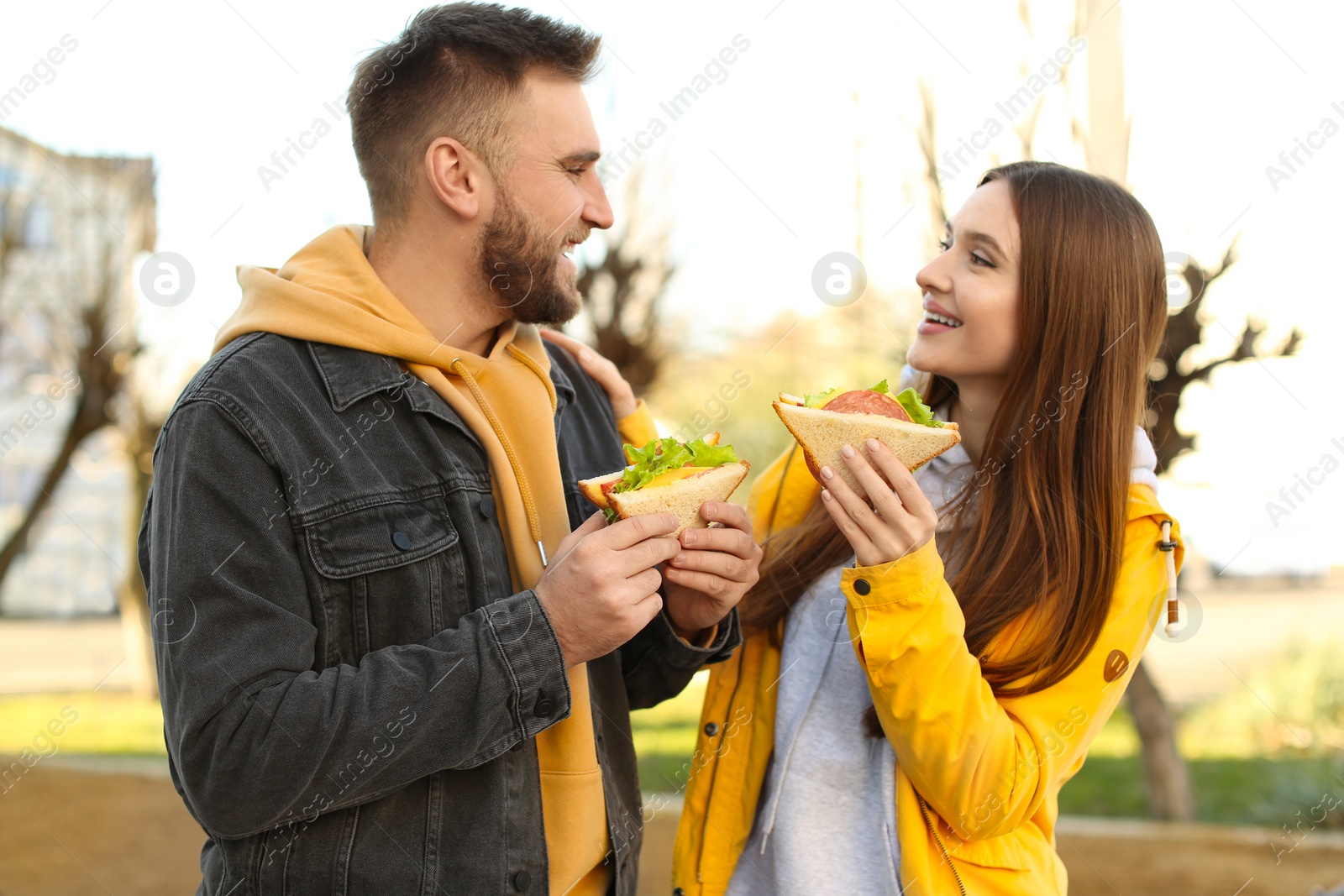 Photo of Happy young couple with sandwiches on city street