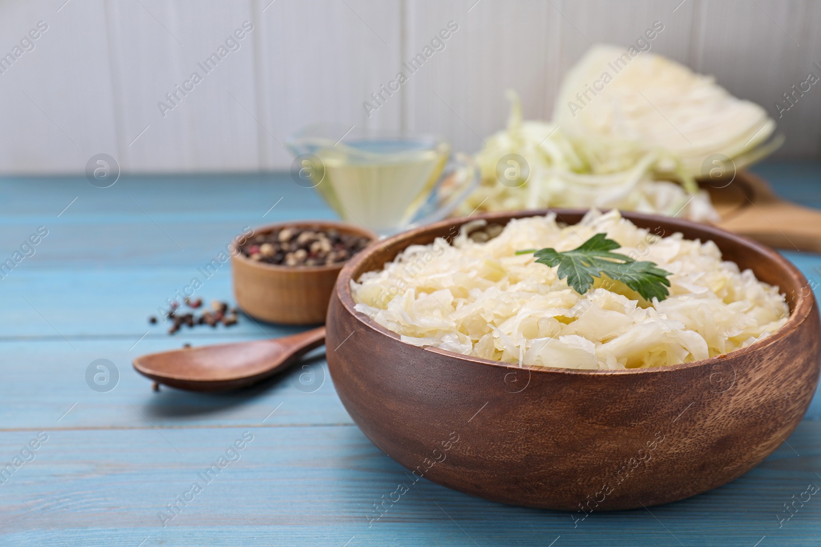 Photo of Bowl of tasty sauerkraut on light blue wooden table, closeup. Space for text