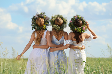 Photo of Young women wearing wreaths made of beautiful flowers in field on sunny day, back view