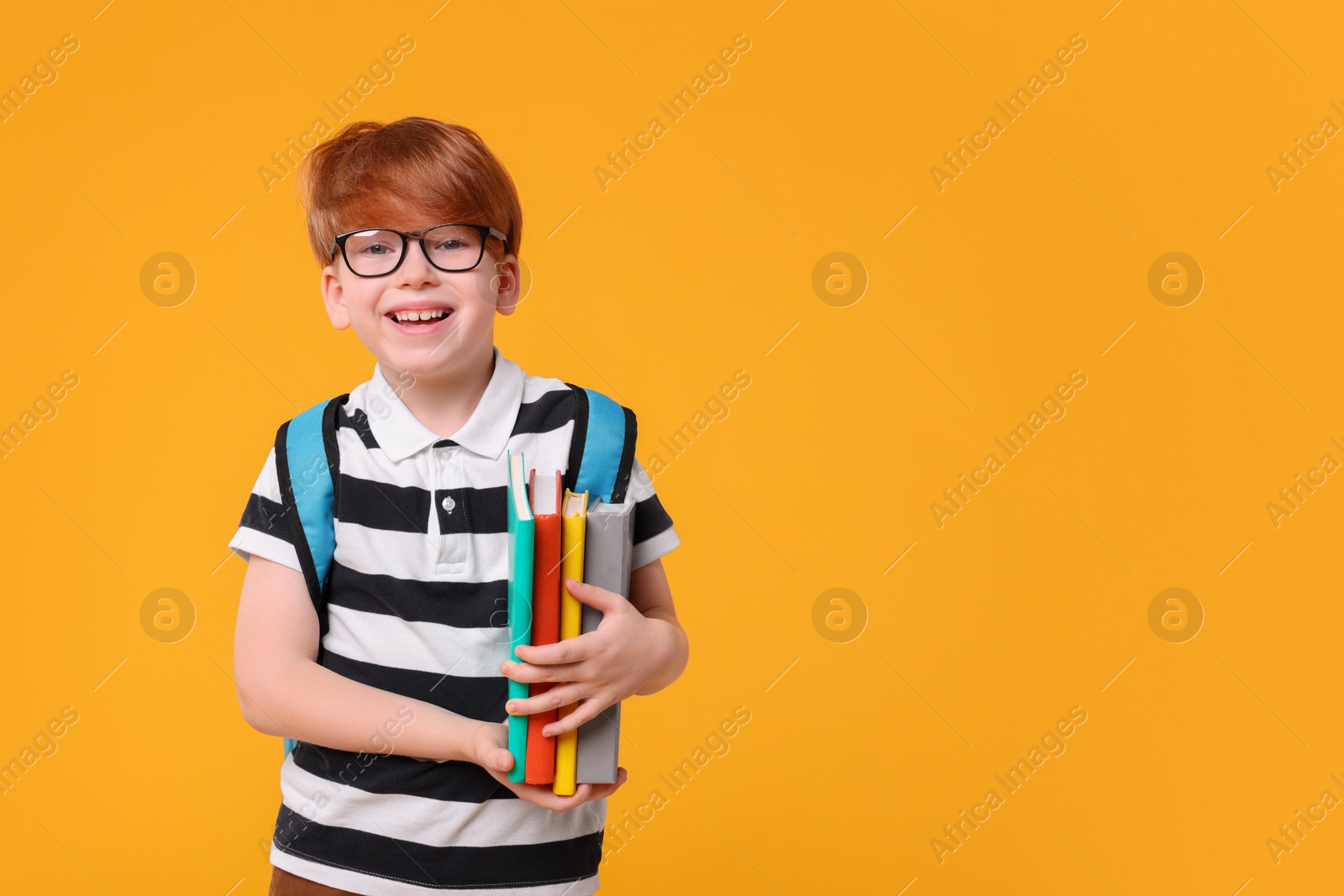 Photo of Happy schoolboy with backpack and books on orange background. Space for text