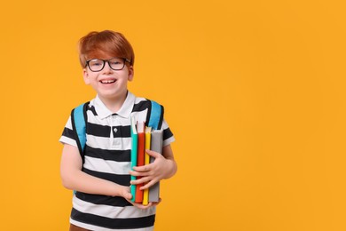 Photo of Happy schoolboy with backpack and books on orange background. Space for text