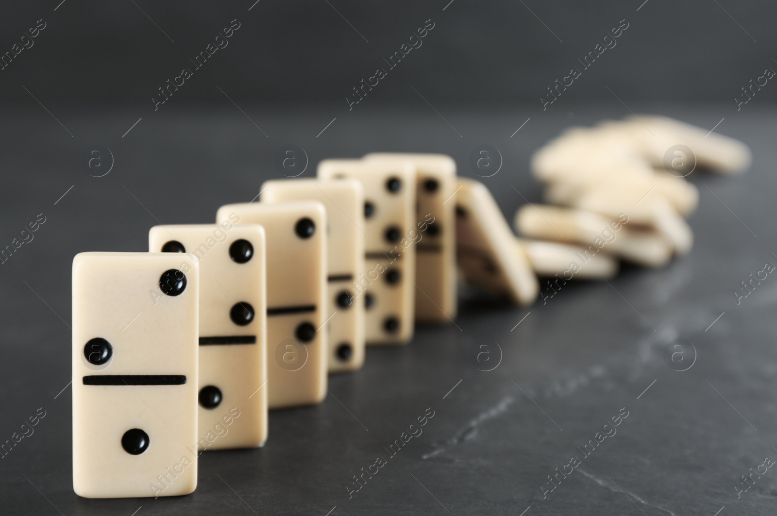 Photo of White domino tiles falling on dark grey table