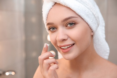 Beautiful woman with towel on head applying face cream in bathroom